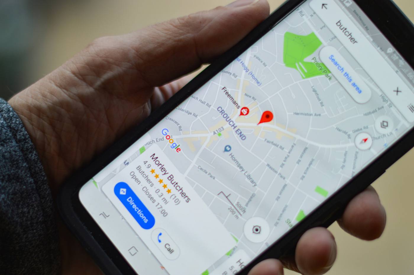 Person holding a smartphone showing Google Maps local search results with a business listing and call button