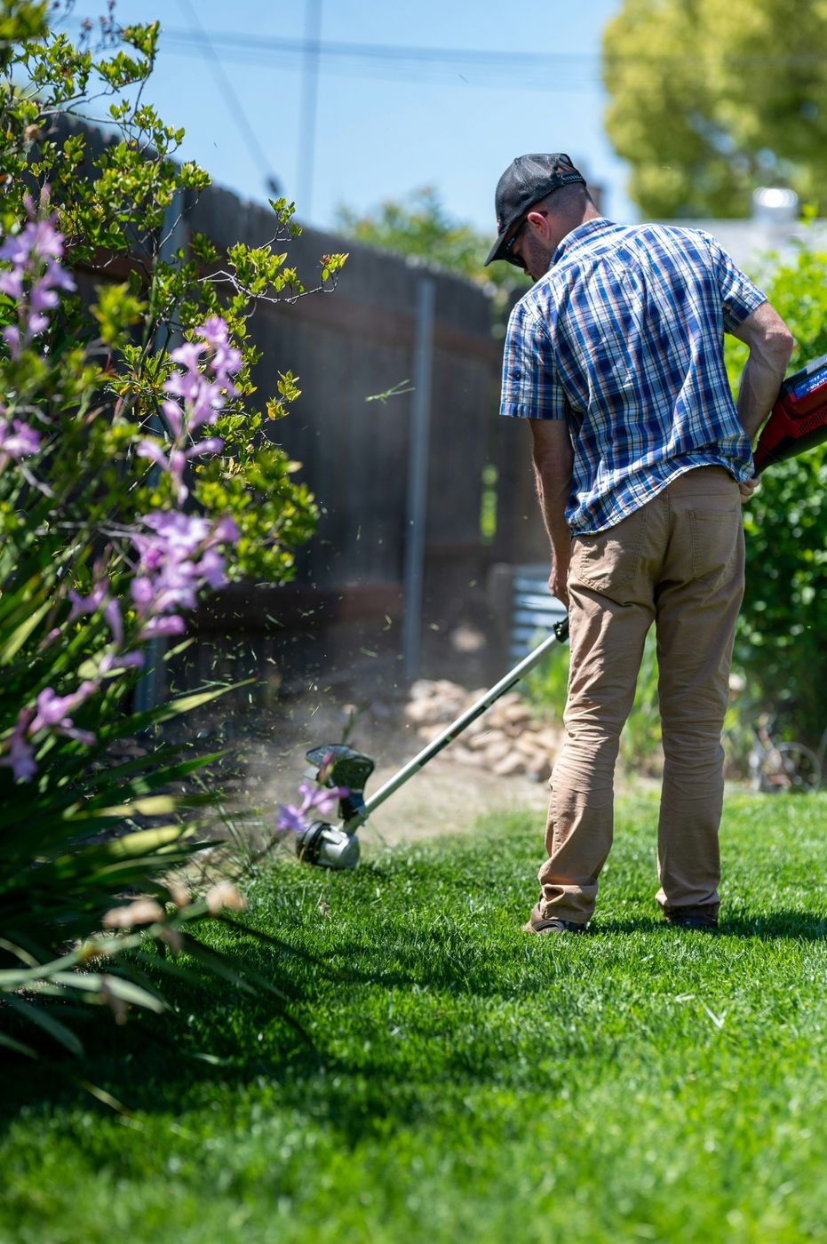 Landscaper using a string trimmer to edge a backyard lawn, an example of local landscaping services customers search for on Google