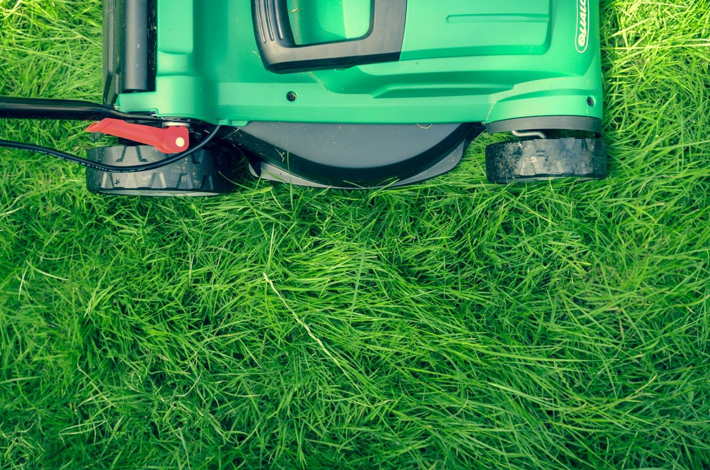 Green electric lawn mower cutting a healthy green lawn, representing local landscaping SEO services